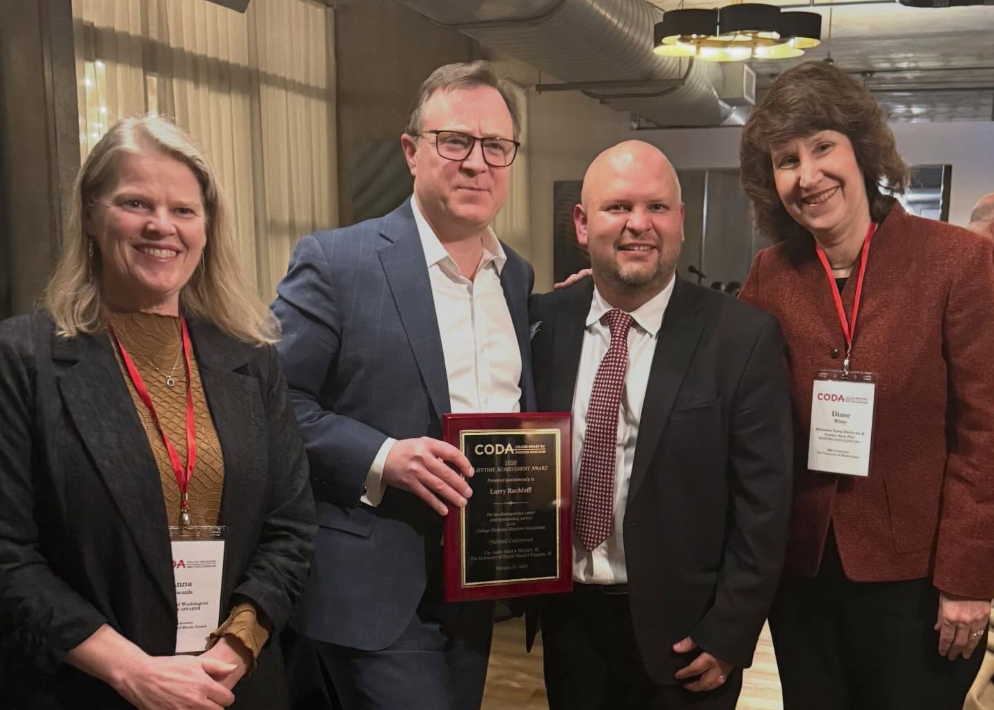 Four people, two men and two women, pose for a photo with Larry's award