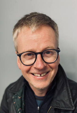 Headshot of a white man in black glasses and wearing a black jacket