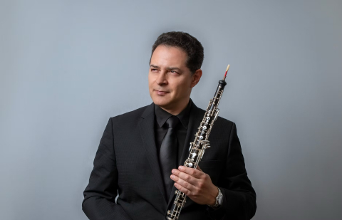 A man in a suit holding an oboe looks off to the side