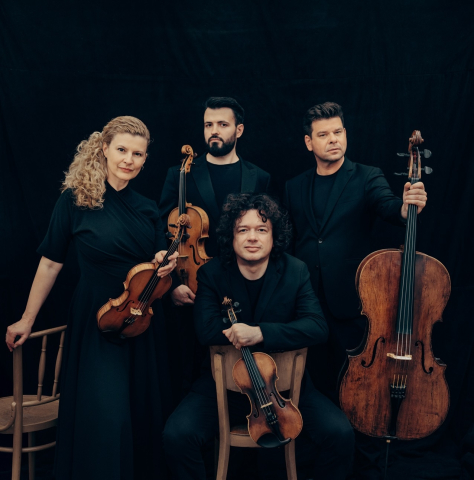 A string quartet in all black poses for a photo, one man sits while the others stand behind him