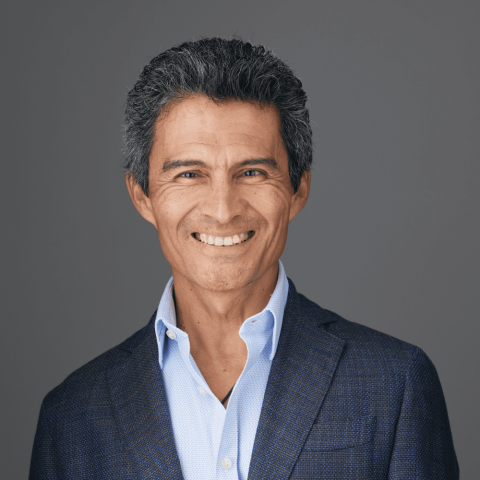 A hispanic man poses for a headshot wearing a blue shirt and suit