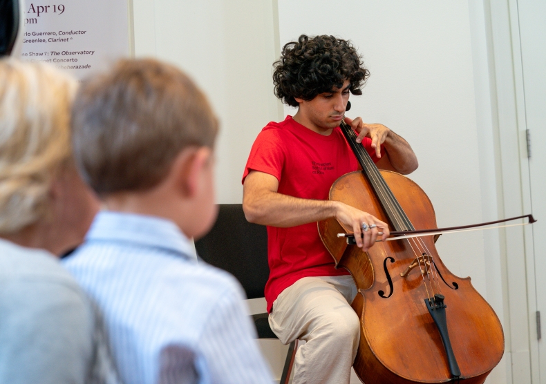 A child and guardian watch a Shepherd School student play the cello