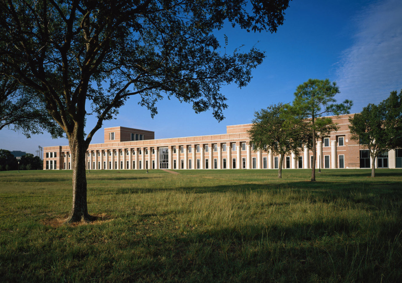A 465-foot long building with columns and bricks, surrounded by grass and a few lush trees