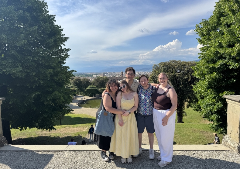 Five students pose in front of a picturesque park with lush trees