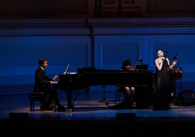 Steven Jamail sits at the piano performing with singer Lea Michele at Carnegie Hall in front of blue lighting