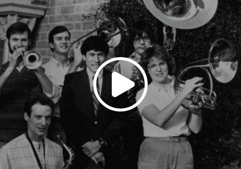 Black-and-white vintage photo of brass students and faculty posing with their instruments; overlaid on top is a play button