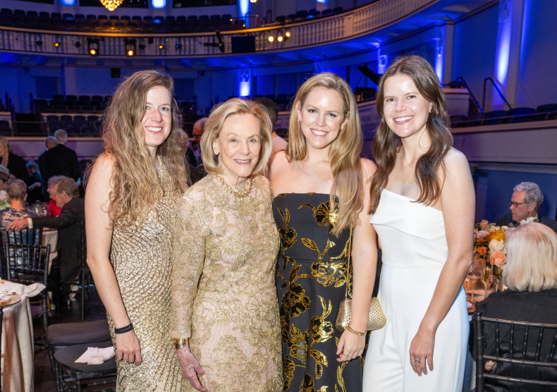 Four white woman wearing fancy gowns smile for a photo in Morrison Theater