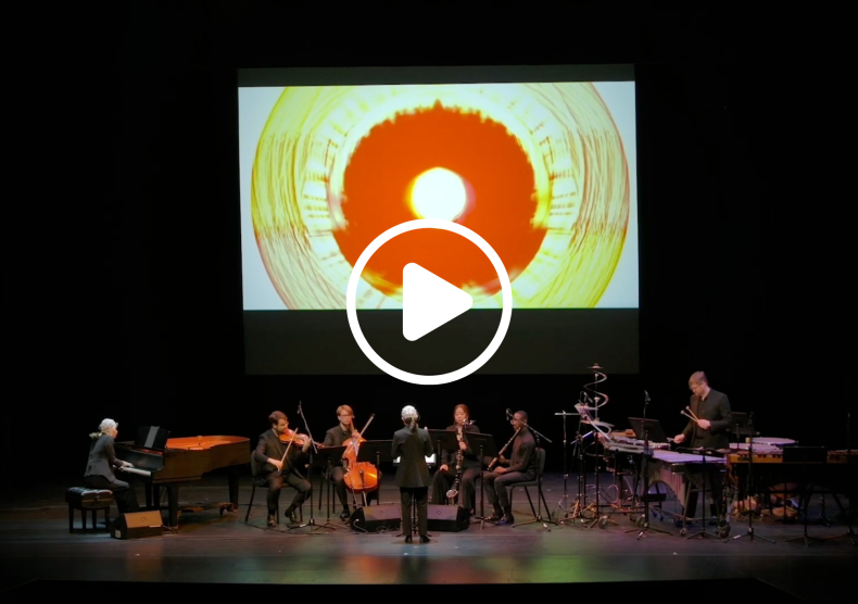 An ensemble of instrumentalists perform in front of a screen with designs