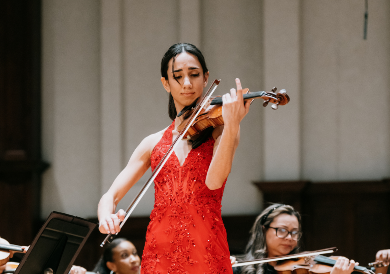 A woman in a red dress performs the violin with orchestra