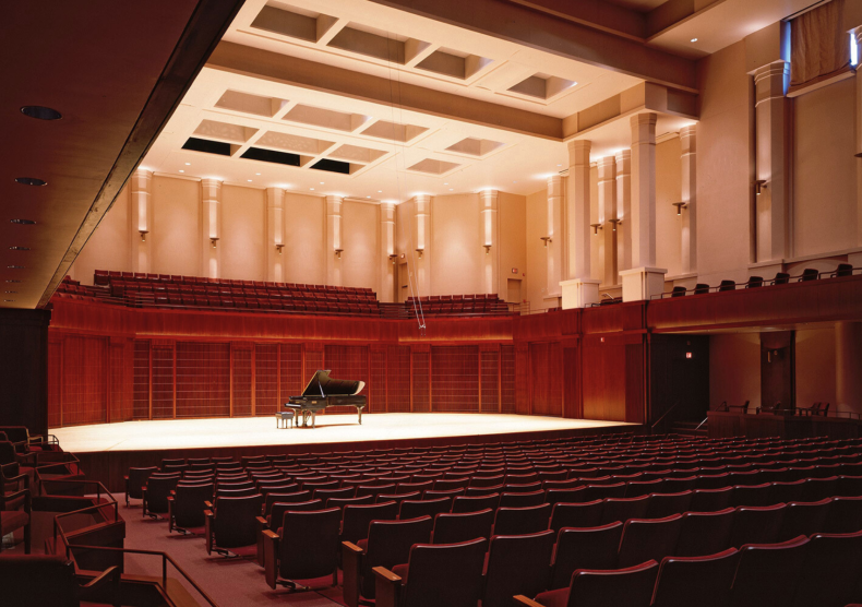 Inside of Stude Concert Hall with warm brown walls and red seats and a grand piano on stage