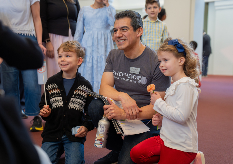 Two young kids smile for a photo with conductor Miguel Harth-Bedoya, one holding a baton and the other holding a flower