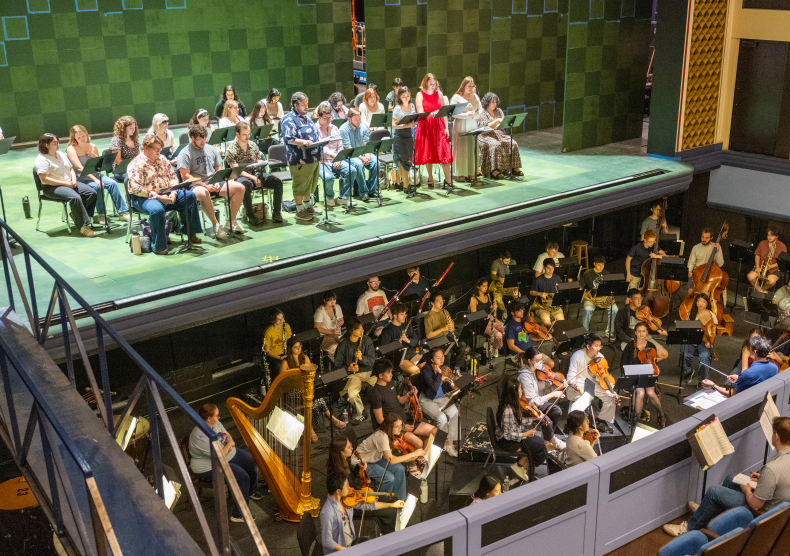 The view of students seated on a green stage at a sitzprobe with the orchestra in front of them in the pit