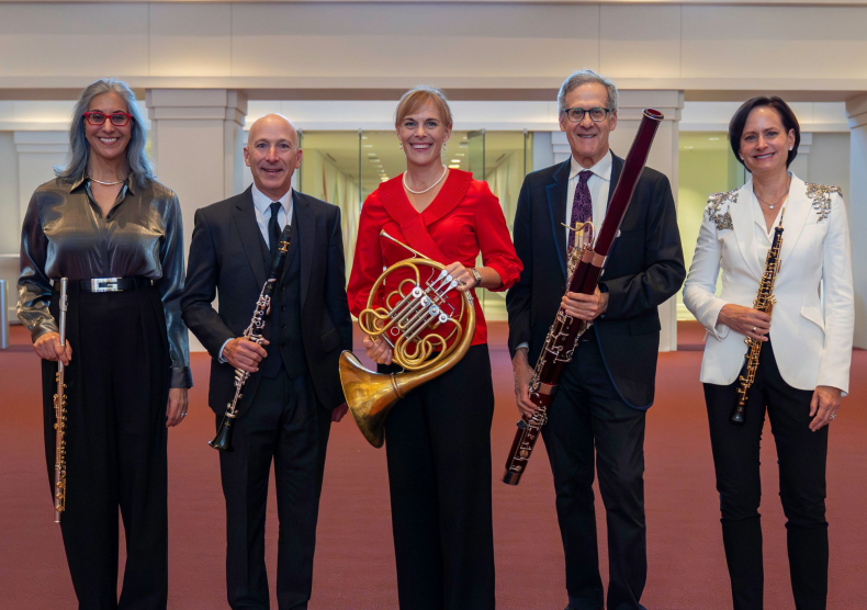 Five faculty in formal attire smile and pose with their woodwind instruments