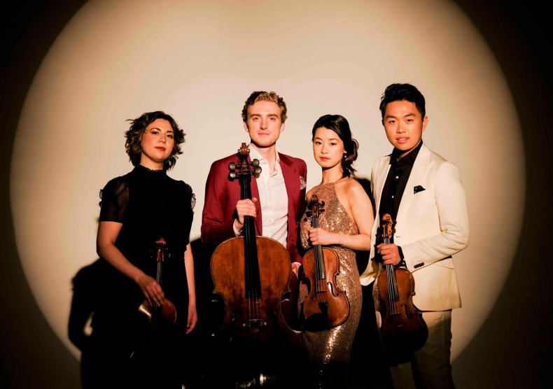 Four musicians of a string quartet stand in front of a bright circular light projection