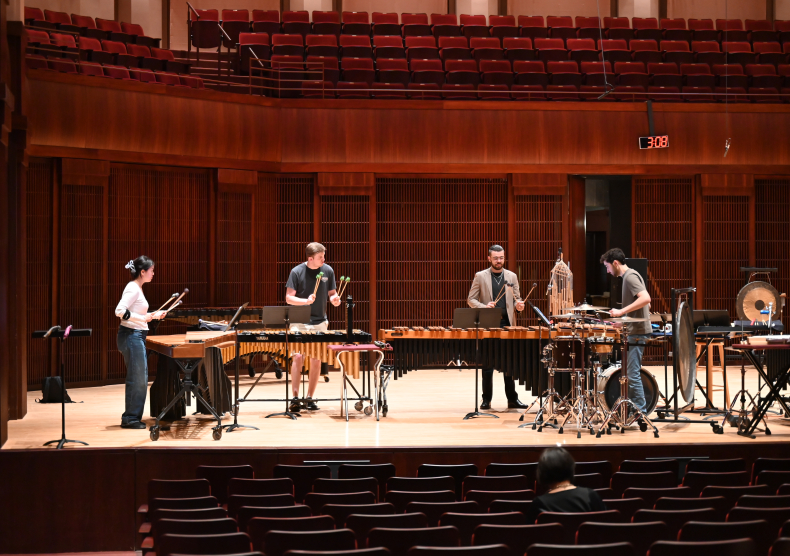 Four percussion students rehearse on stage