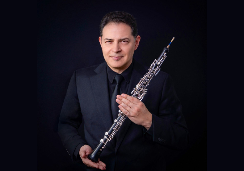 A man in a suit poses for a photo while holding his oboe in front of him