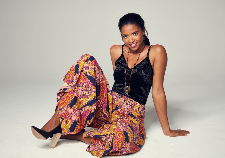 Photo of a woman seated down with a black tank top and colorful pink pants