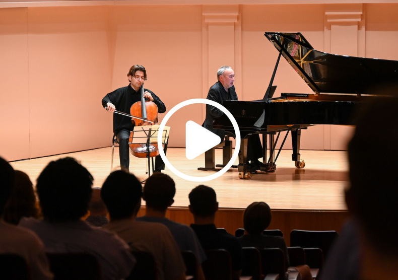 A cellist and pianist perform in an intimate recital for a full audience; there is a video play button overlaid on the image