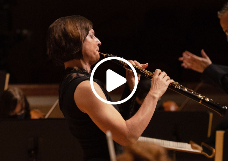 An oboist performs with orchestra; a video play button is overlaid on top the image