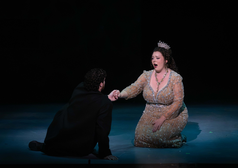 Two singers sit on stage, the woman sings to the man